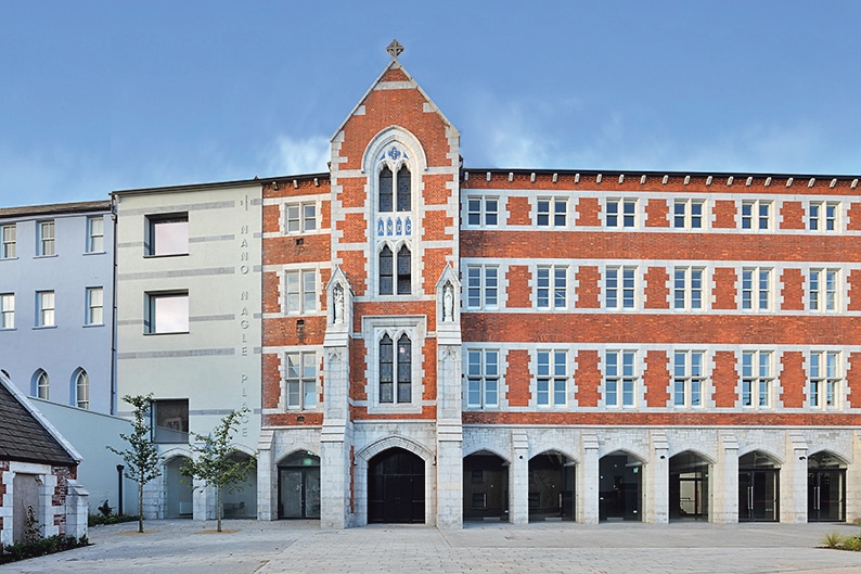 The red-brick courtyard buildings at Nano Nagle Place in Cork, with arched doorways, Gothic-style windows and pale stone detailing.